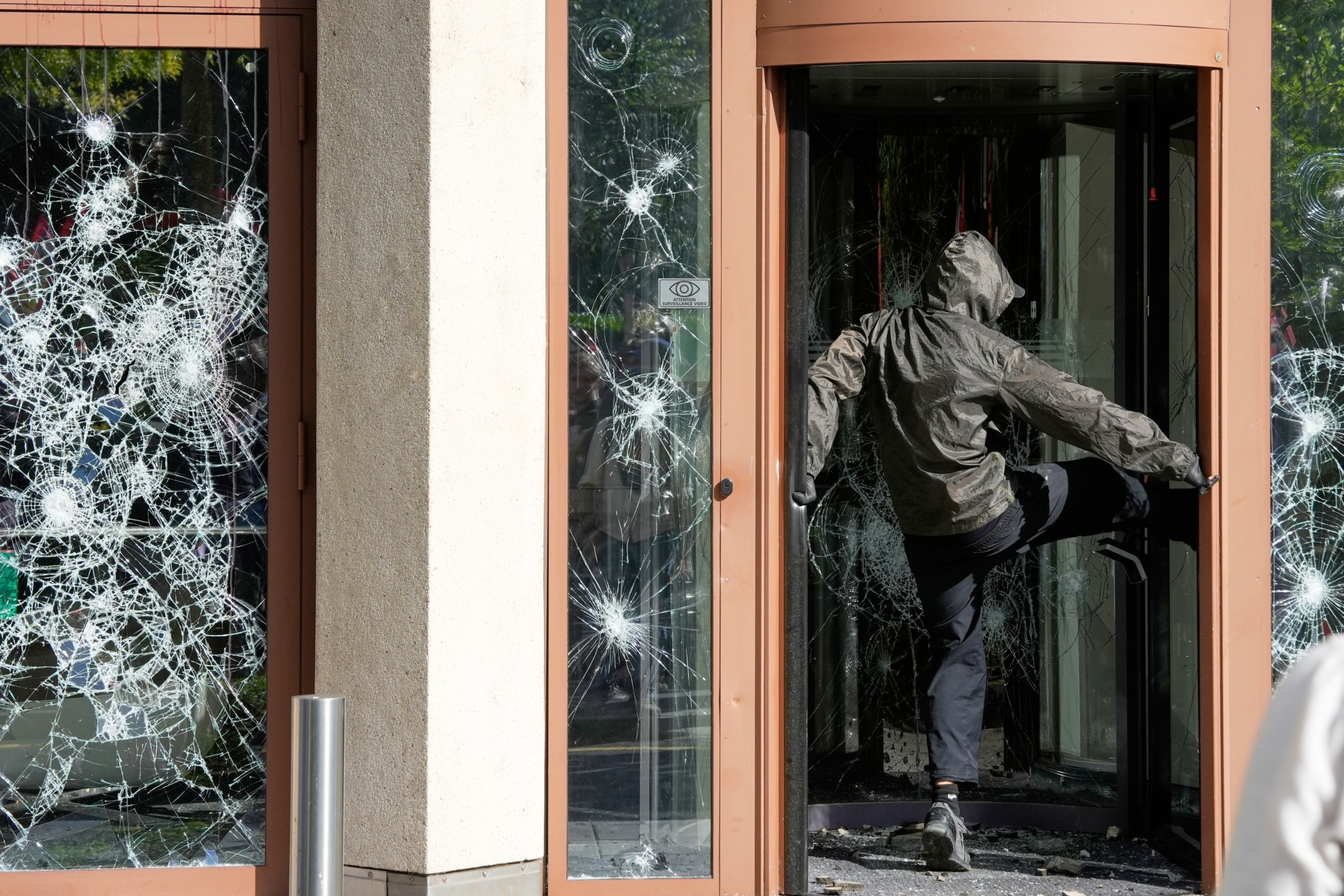 A protester kicks at a window during a "No G7" demonstration in Geneva, Switzerland, Sunday, June 14, 2026, ahead of the G7 summit scheduled to take place June 15-17. (AP Photo/Baz Ratner)